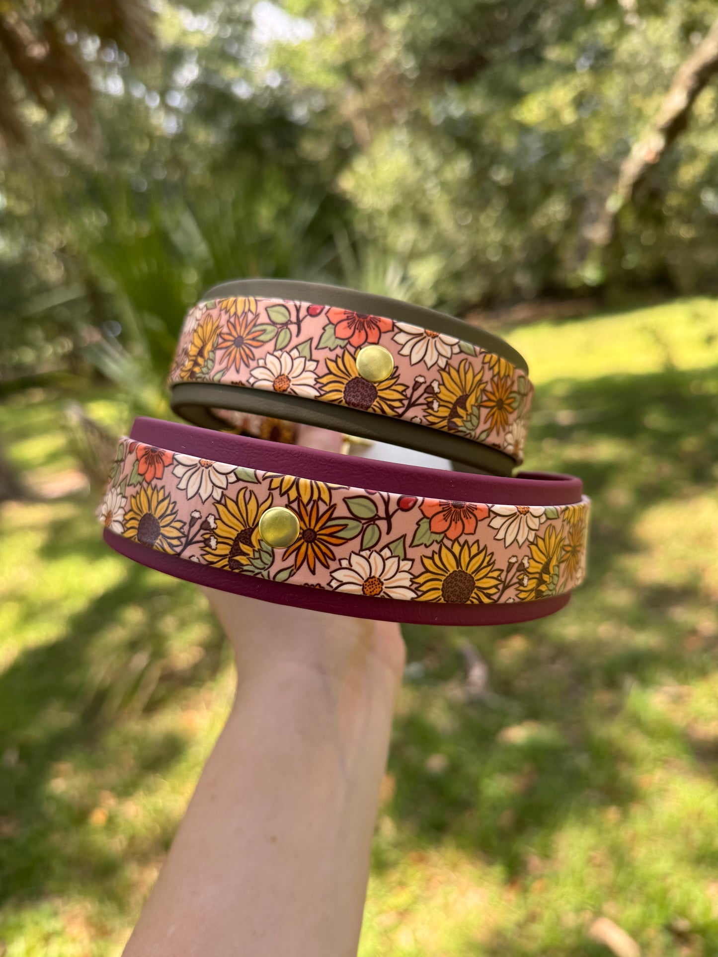 A dog collar with a floral pattern. gold-tone hardware, held infront of a blurred green background