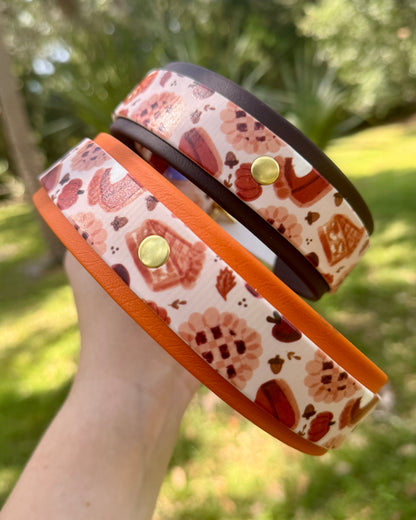 Two biothane dog collars with a red and orange pie pattern held with a blurred green background