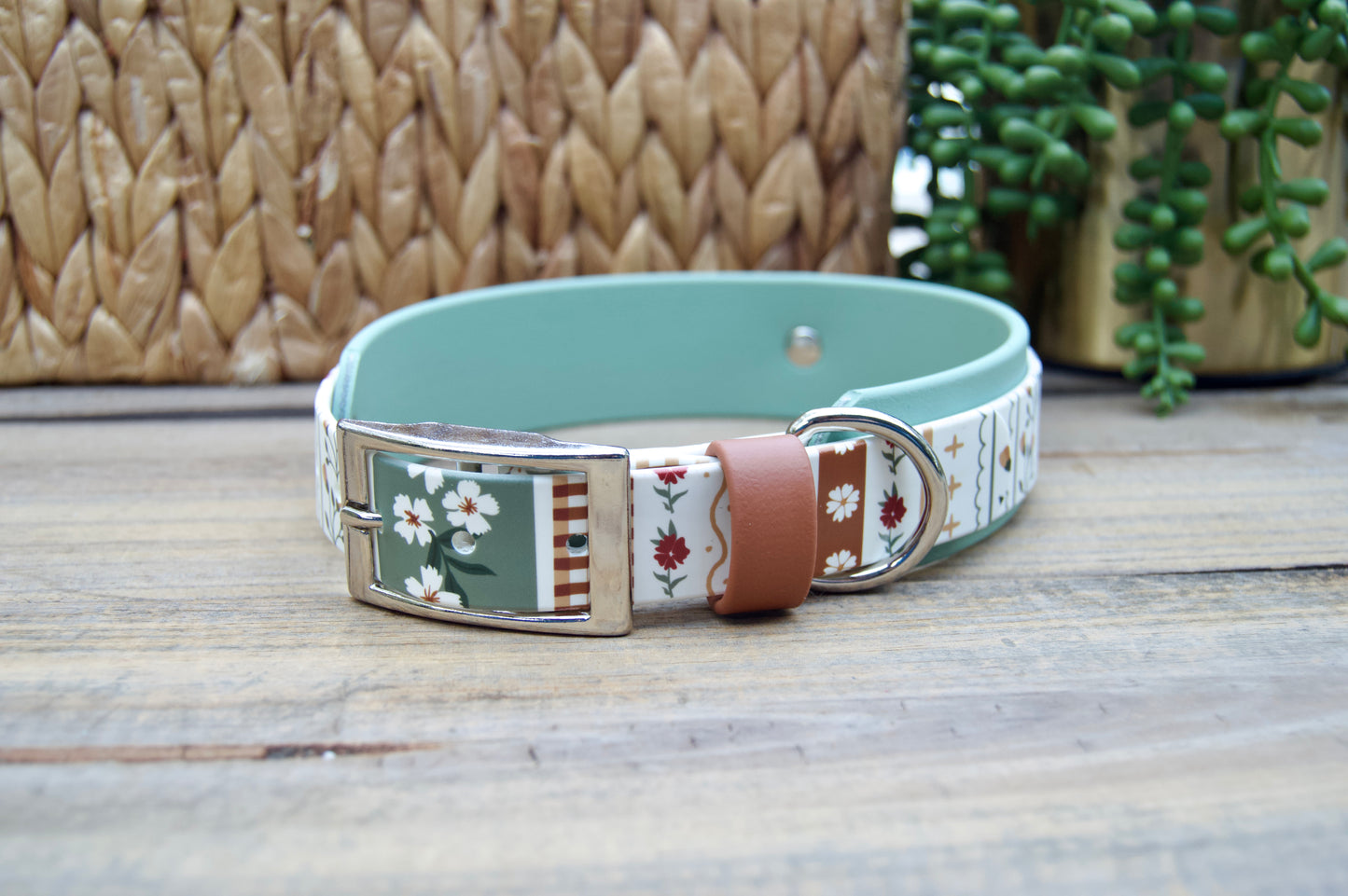 biothane dog collar with a striping floral design and sage green accent on a wooden surface with a natural basket and plant in the backgrounds