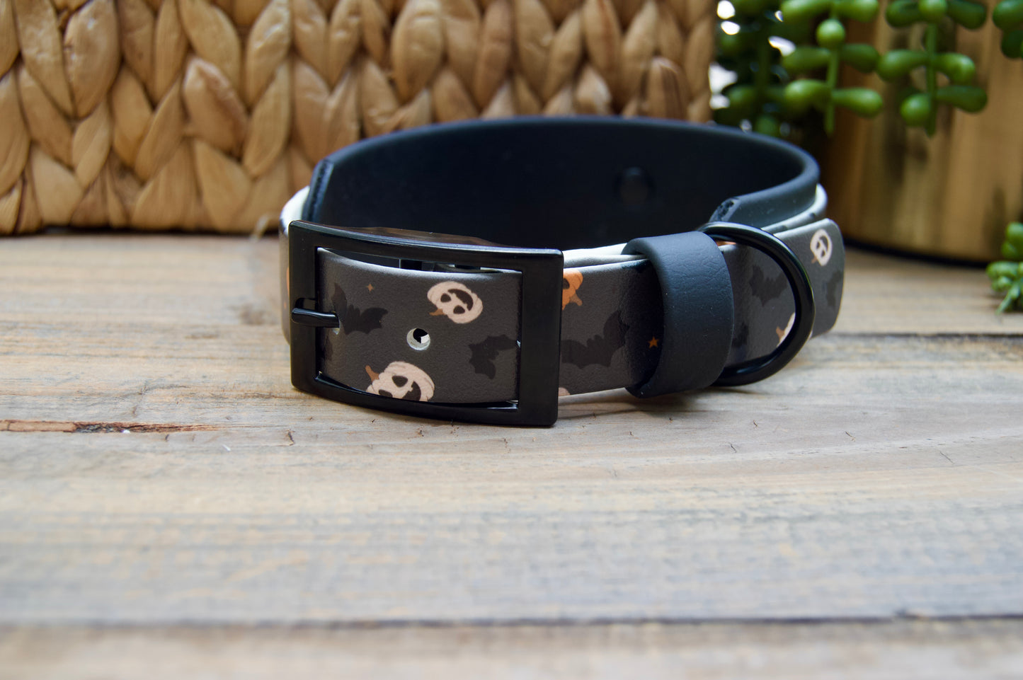A black dog collar with a Halloween-themed print of bats and jack-o'-lanterns, resting on a rustic wooden surface.