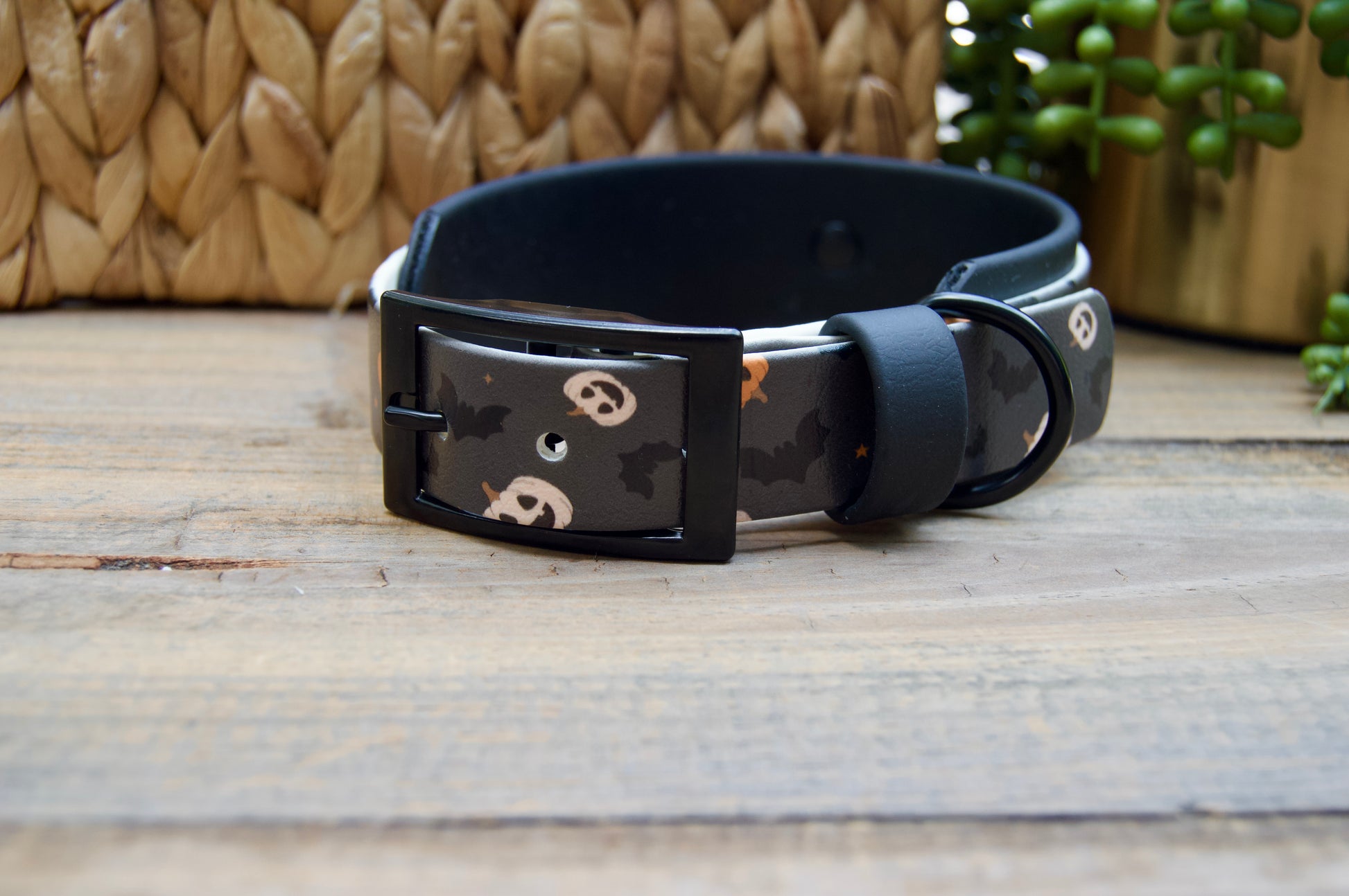A black dog collar with a Halloween-themed print of bats and jack-o'-lanterns, resting on a rustic wooden surface.