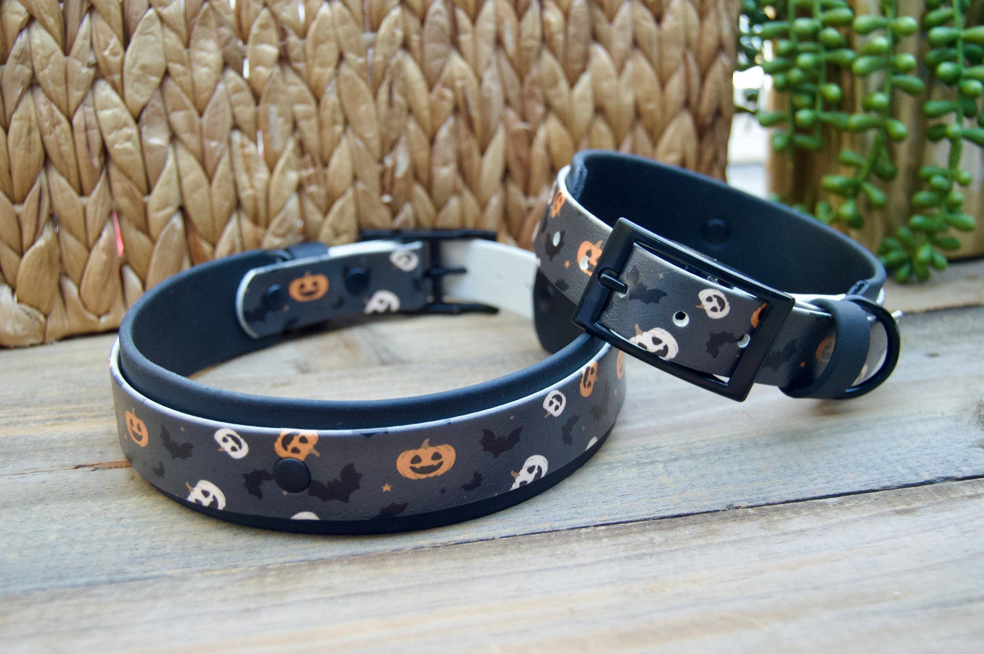 Two Halloween-themed dog collars on a wooden surface with a woven basket background.